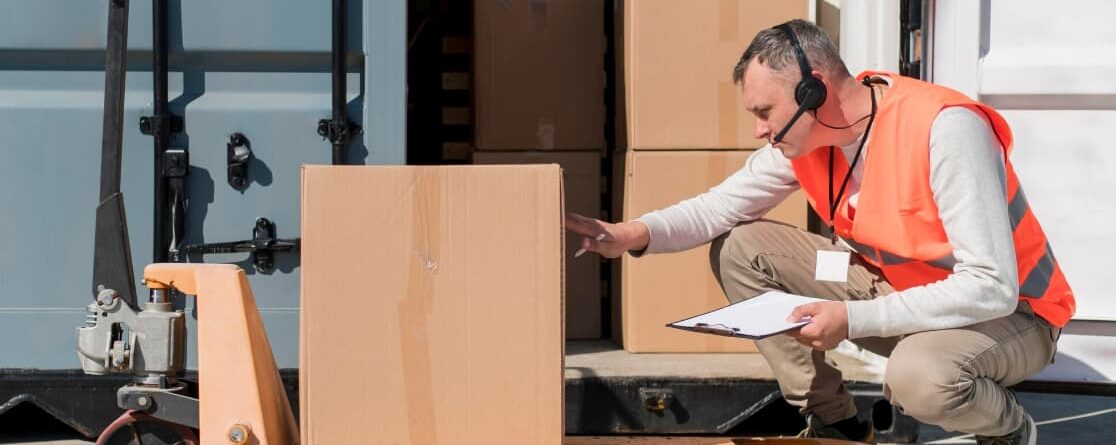 a man wearing headphones and holding a clipboard next to a hand truck