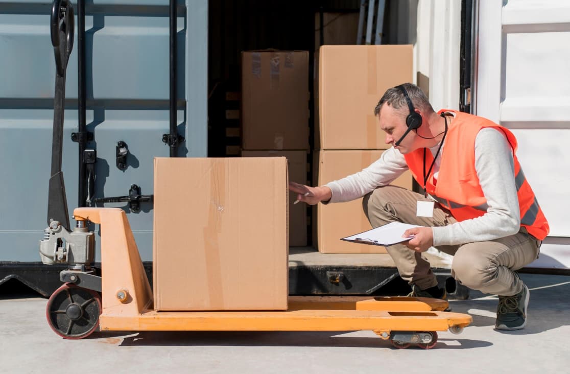 a man wearing headphones and holding a clipboard next to a hand truck